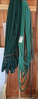 Folded green patio umbrella and coiled garden hose hanging beside each other