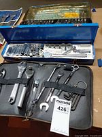 Overall view of three tool containers: plastic socket set, blue metal socket box, black zip pouch with hand tools
