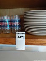 Stack of white plates next to patterned tumblers on shelf