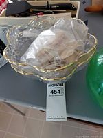 clear scalloped plastic bowl with gold trim containing seashell bag