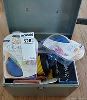 Open metal lock box showing OFF! clip-on packs, flashlight, Vidal Sassoon box, brushes, hardware