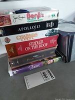 Stack of six VHS tapes with titles visible plus partial view of other cases