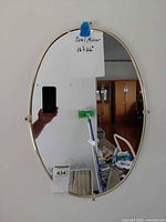 Front view of oval gold/brass wall mirror with mounting hardware visible