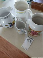 All four pitchers grouped on tabletop showing designs and relative sizes