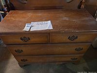 Front view of solid wood dresser with scratches, headboard of bed frame visible behind