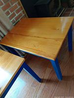 Top and legs of one square table showing natural wood top and blue legs