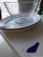 Clear glass bowl resting atop stacked white gold-rim dinner plates on counter