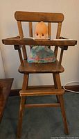 Front view of wooden doll high chair with doll seated