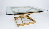 Full view of square glass coffee table showing glass top and brass-tone X-base