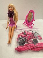 Barbie doll seated beside mirror and bagged accessories