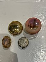 Four pill boxes laid out: gold-tone round, pink Pisa souvenir, oval portrait, silver-tone embossed