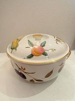 Side view of round porcelain casserole with lid, showing fruit motifs and gold trim