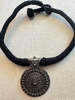 Full view of necklace showing black cord and round silver pendant
