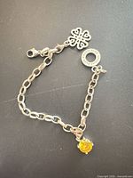 Full view of bracelet showing chain, clasp, engraved ring and yellow stone charm