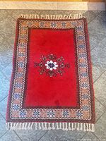 Full view of red wool rug with fringe and border pattern