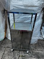 Full front view of stainless steel cart showing top, open shelf, lower cabinet, and casters
