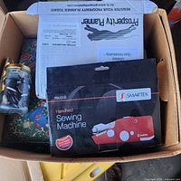 Box showing Swartek handheld sewing machine, glass jar of notions, quilted pouch