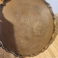 Front of smaller brass tray showing scalloped rim and etched figures