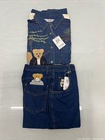 Folded denim shirt and jeans showing tags and teddy bear motifs
