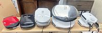 Five countertop appliances lined up: four George Foreman grills and one additional white unit