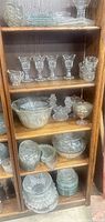 Shelves showing majority of pressed glass items including dessert glasses, creamer, large bowl, figurines, nested bowls and plates
