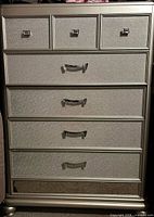 Front view of silver six-drawer tall chest showing drawer arrangement and mirrored panel