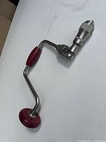 Full view of steel brace hand drill showing red wood handles and chuck