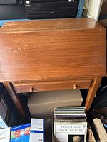 Front view of closed wooden drop-front desk, shows drawer and overall form