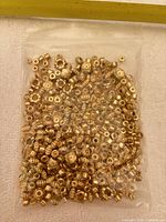 Sealed plastic bag filled with small gold-tone plastic spacer beads