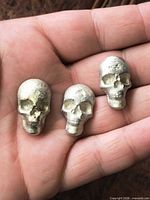 Three small silver-tone skull knobs in hand for scale