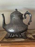 Front view showing engraved body, handle, spout, feet