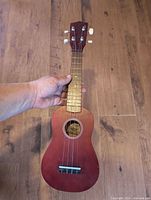 Front view of wine red soprano ukulele showing body, neck, fretboard, strings, bridge and soundhole label