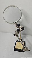 Front view of helping hand magnifier showing lens, arms, clips and base