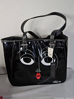 Front view of black vinyl tote showing graphic face and attached tag