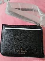 Front view of black Kate Spade card holder showing gold logo and wrist strap wrapped in foam