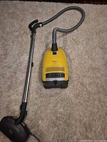 Full view of vacuum canister attached to hose, wand and floor head on carpet