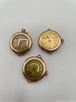 Front view of all three gold-tone pendant watches displaying dials and bow loops