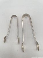 Two sterling silver tongs side by side showing size difference