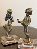 two silver-tone figurines on acrylic bases