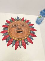 Front view of terracotta sun face plaque beside water bottle for scale