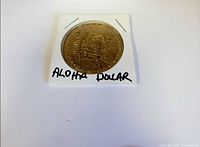 Front of brass-tone Aloha Dollar token in holder