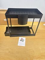 Front view of assembled black two-tier storage caddy with drawer, cup attachment, hardware and instruction sheet