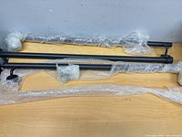 Two matte black rods and brackets wrapped in bubble wrap on tabletop