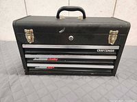 Front view showing three drawers, logos, latches and handle