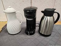 Three items: black Frigidaire coffee maker centered, white ceramic carafe left, stainless steel thermal carafe right