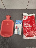 All three items laid out: loose red hot water bottle, Vital Health toothbrush kit, sealed Life hot water bottle