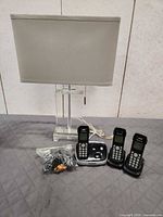 Overall lot showing three cordless phones in cradles, main base, acrylic base table lamp and bag of accessories