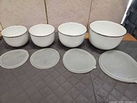 Four white enamel bowls and four lids laid out to show sizes