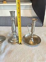 two matching candlesticks beside brass chamberstick, measuring tape for scale
