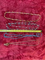 Four strand necklaces including gold-tone chain with pendant, amber, light blue and turquoise bead strands laid next to measuring tape
